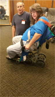 Figure 3 Left is a side view of a non-ambulatory large female seated in an Columbia Aislemaster boarding chair. The person is not able to be secured in the boarding chair. The person is hanging over the seat. The straps are not able to be positioned properly. The foldable arm supports cannot be moved down into the usable position because they will not fit this person’s girth.