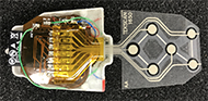 Six circular force sensitive resistors (FSRs) are arranged on a small polyester film measuring 3 cm wide by 3.4 cm long. Four FSRs arranged in a diamond pattern are used for directional control with two sensors side-by-side used for right and left mouse buttons. Leads from the FSRs come together in a tail and are soldered to a flexible PCB.