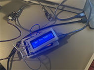 The device is in a more final state. It has an liquid crystal display that flashes 'Hi, I'm TOASTI!' upon start-up. It also has a white, 3D-printed casing. The circuit board can be separated from the LCD through the use of Velcro straps that are mounted on the casing.
