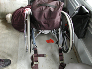 Post-crash photo taken from behind the wheelchair in case WC-006 showing the deceased occupant lying on the floor of the van in front of the wheelchair.  The deceased occupant&rsquo;s head is toward the center of the van and the occupant is lying on her left side.