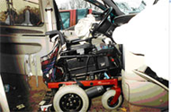 Side view of the driver&rsquo;s wheelchair in case WC-014 secured in the docking tiedown device, with the deployed steering-wheel airbag draped into the wheelchair seat.