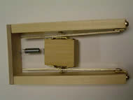 Image shows the overhead view of the mechanical track demonstration of principle constructed using a wooden skeleton with metal components. Two &frac12;” X 2” X 10” pieces of poplar wood serve as the track support pieces with a sliding track attached to each one. A smaller wooden piece, the pick-holding component, lies in between the tracks suspended through screw connections. A spring links the pick-holding component to a wooden end piece, perpendicularly attached to both track support pieces.