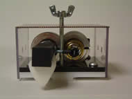 Image shows the front view of the strumming component. A mounting plate and a base plate are screwed together. The push and pull solenoids are enclosed in circular clamps and attached onto the base plates. The pick rod connected to the push solenoid plunger is connected to the pull solenoid plunger through a screw connection extending between both solenoids parallel to the base plates. 