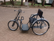 This figure shows the third generation of the Figure-Eight Drive installed on a standard APDK handcycle, in Nairobi, Kenya.  The system only requires modification of the tricycle’s fork and chains, leaving the rest identical to single-speed models. 