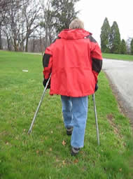 This photo shows the prototype crutches being used on a cross slope, a grassy hillside. The left crutch is shorter than the right because the ground slopes down to the right. 